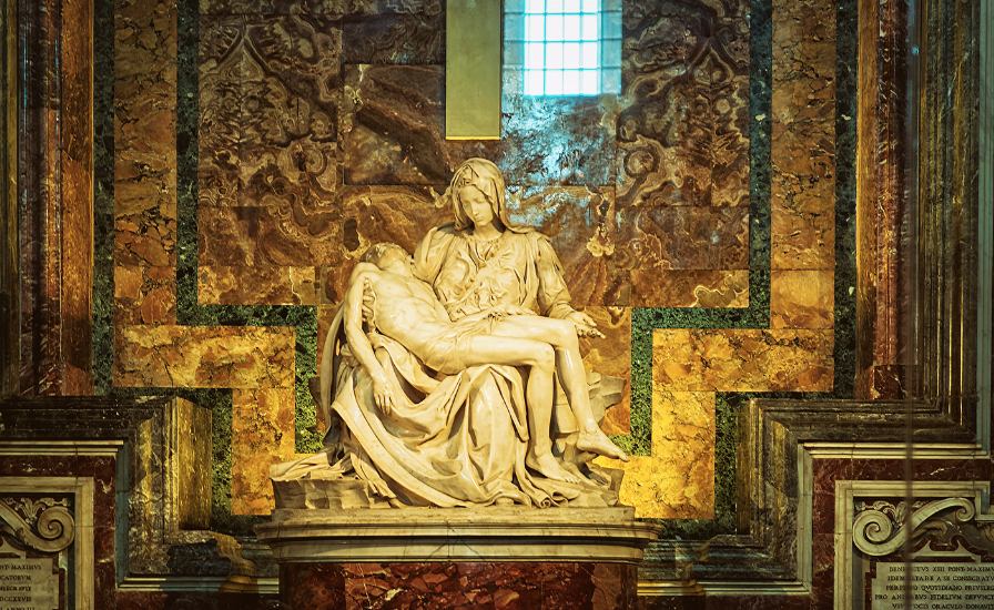 Statue of the Virgin seated on a pedestal, serene expression, hands folded in prayer.

